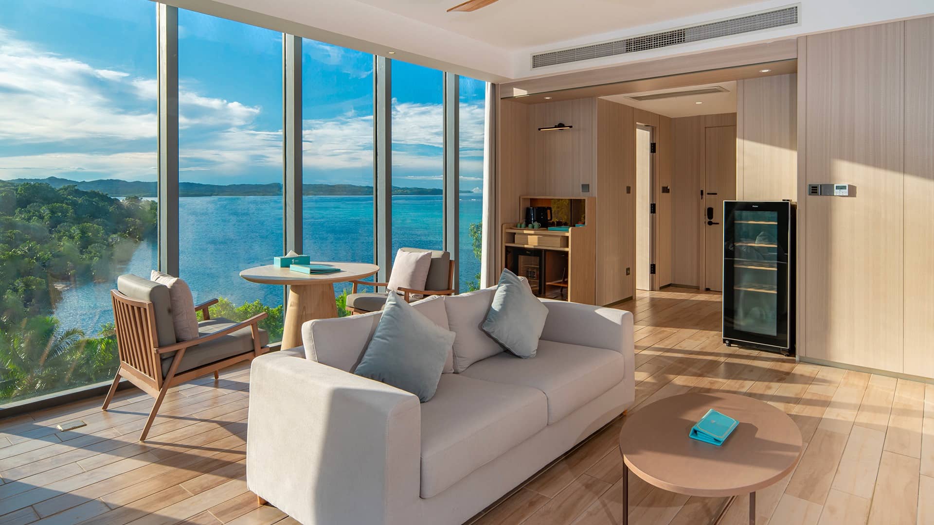 Luxurious Signature Sunrise Suite living area with panoramic ocean and jungle views, modern furnishings, kitchenette, and floor-to-ceiling windows